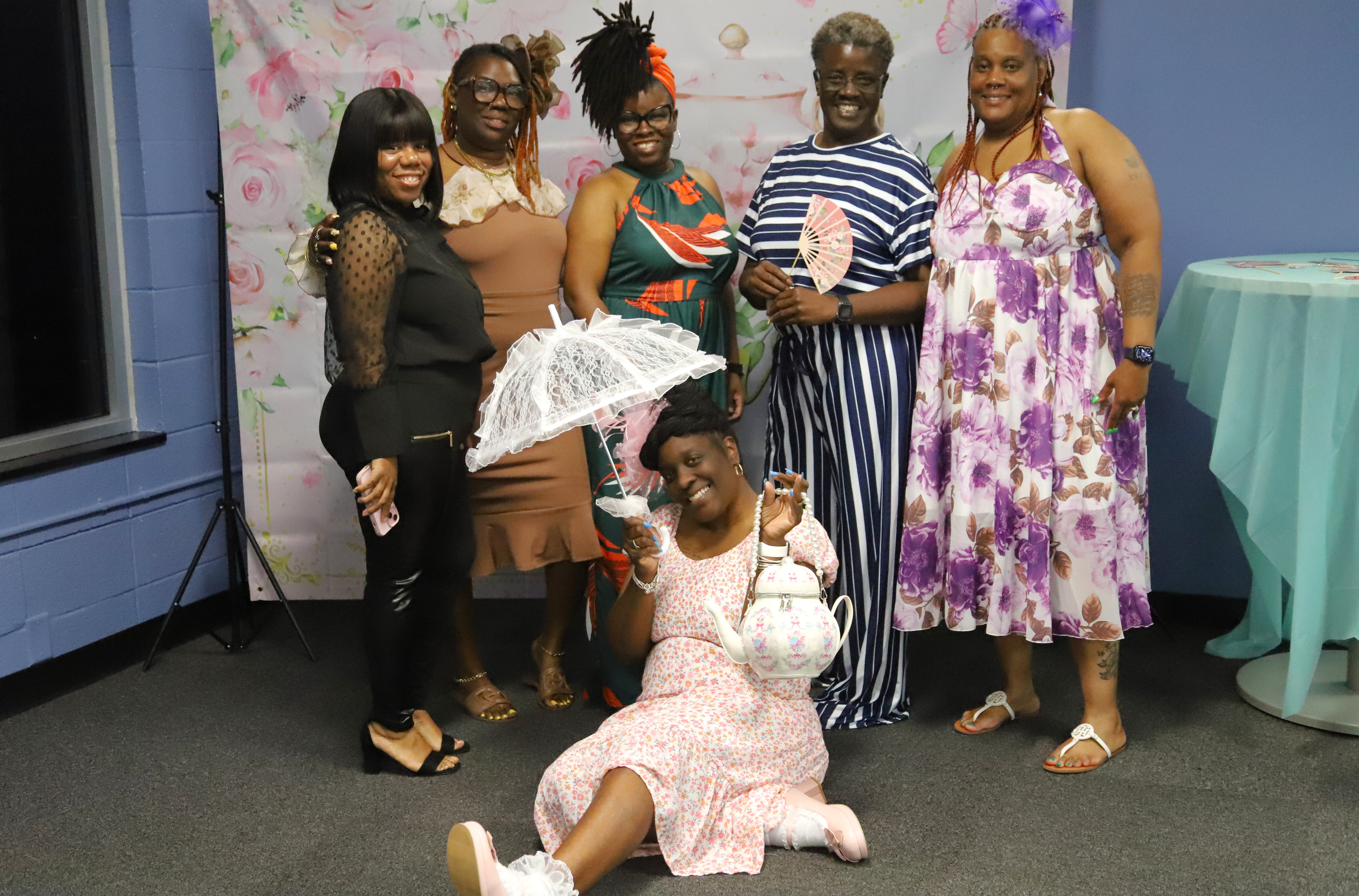 Six women in playful dress-up hats and accessories posing at a Smart Start ladies' tea event