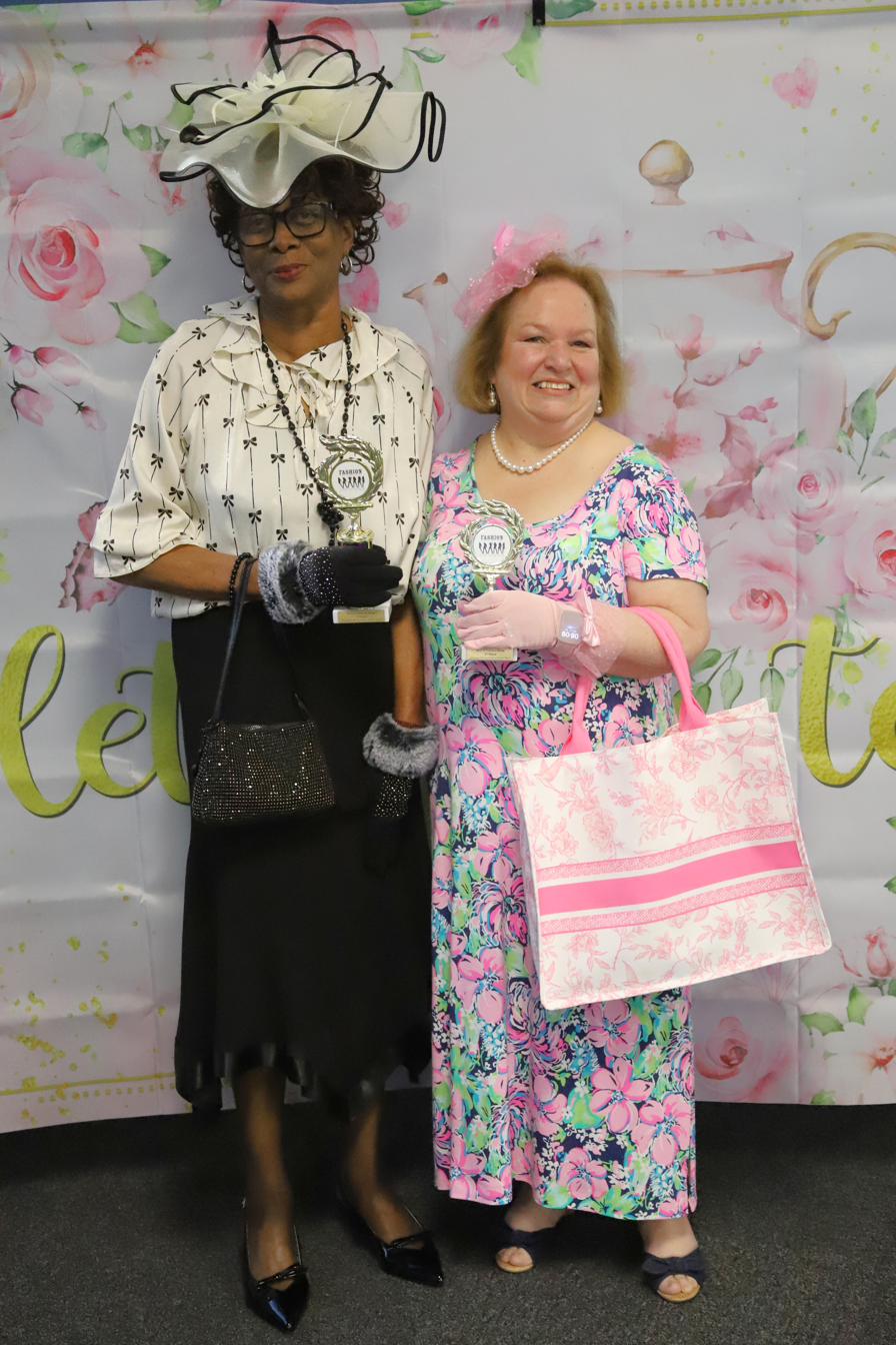 Two women dressed up in decorative hats holding fashion show trophies